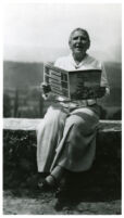 Gertrude Stein, seated on wall reading magazine