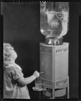 Photograph of Little girl getting a glass of water from a Puritas water dispenser, Los Angeles, between 1935