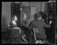 Woman speaking at a sound stage or radio station with a technician at the controls, 1930-1950