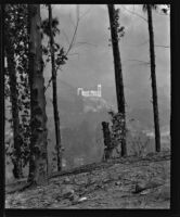 View across a canyon towards a large building on a slope, circa 1920