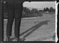 Legs of man standing on a narrow paved road, circa 1920