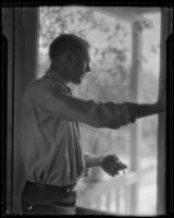 Unidentified man looking out a screen door, circa 1920