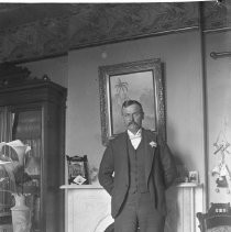 View of a man standing in front of a fire place. Vase of flowers is on the left
