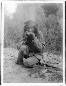 Old Havasupai Indian man crouching on the ground, putting something in his mouth, ca.1900