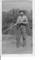 Daniel Webster holding rifle in jeans, shirt and hat
