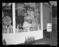 Man looking out a gas station window upon which is written "CHOKE THE JAPS WITH YOUR GIRDLES WE WANT RUBBER" in 1942, Los Angeles, Calif