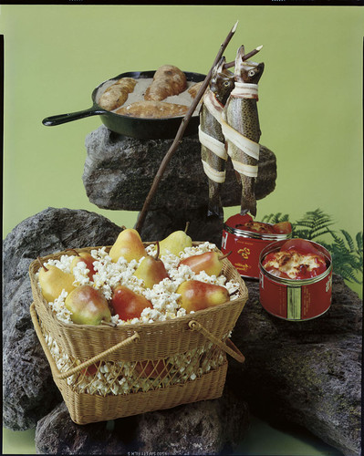 A basket of popcorn with pears, two trout and a cast iron frying pan with potatoes