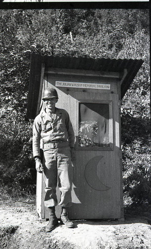 Corporal posing in front of an outhouse