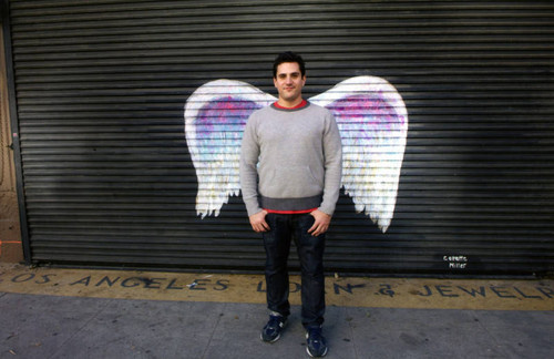Unidentified man in grey sweater posing in front of a mural depicting angel wings