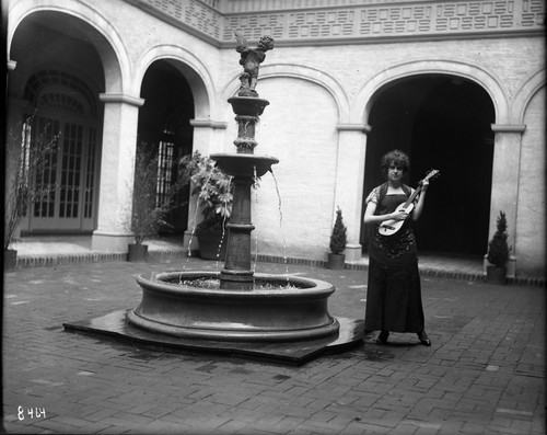 Miss Brand, standing by a fountain, playing a stringed instrument