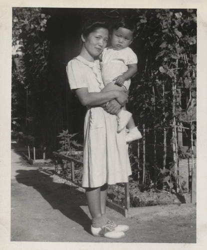 Woman holds a little boy next to trees at Poston incarceration camp