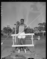 Rafer Johnson poses with track and field equipment