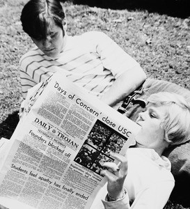 Two students lying on the lawn with one reading the Daily Trojan with "'Days of concern' close USC" as the top headline, 1970