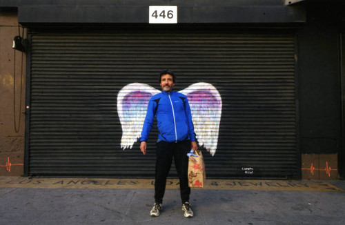 Unidentified man in a blue jacket posing in front of a mural depicting angel wings