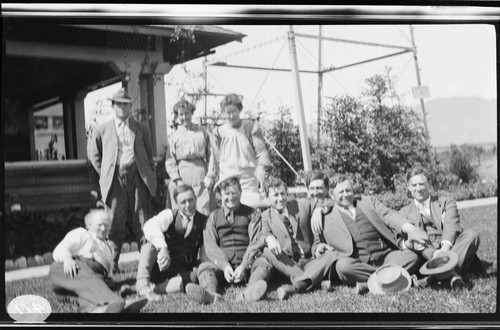 A group portrait of an unknown group of people sitting on the grass by a porch near a transmission tower