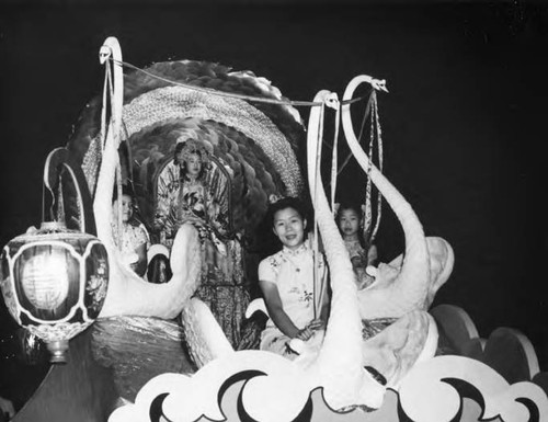 Margaret Kwan Lee, Moon Festival Queen, seated on a float in the Moon Festival procession. She is accompanied by three young women seated on large fake swans