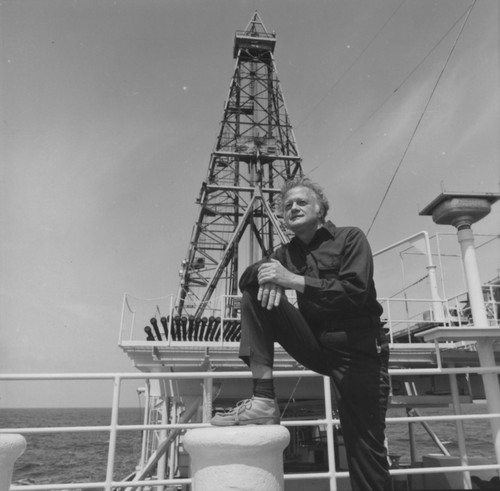 Geochemist John Hunt from Woods Hole Oceanographic Institution, Massachusetts, rests in the bow section of D/V Glomar Challenger (ship) on Leg 42B of the Deep Sea Drilling Project after completing his daily jogging routine. In the background is the 194-foot tall drilling derrick. The managing institution for Deep Sea Drilling Project was Scripps Institution of Oceanography under contract to the National Science Foundation (NSF). 1975