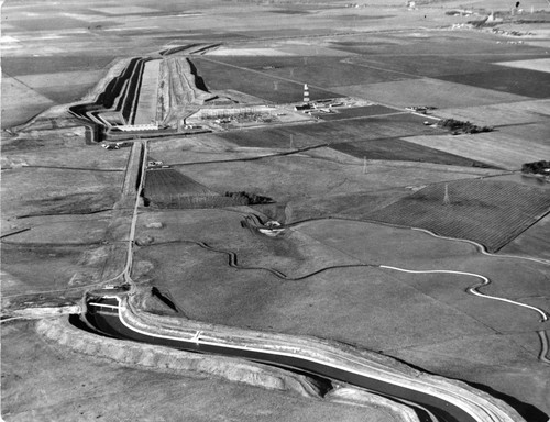 31 This is an aerial view of the Tracy Pumping Plant area which is the beginning of the Delta Mendota Canal. The upper right hand corner of the photograph shows the beginning of the inlet canal. Water is diverted from the Old River into the inlet canal which follows into the Tracy Pumping Plant. When water enters the pumping plant it is pumped up-hill for approximately one mile. This process lifts the water 200 feet so that it can start its gravity drain down the canal