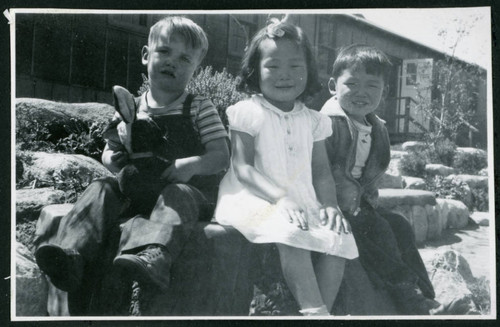 Photograph of children sitting on a bench in front of the Manzanar hospital