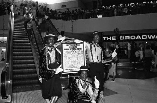 Young men in costume posing with a Black History Month sign at a mall, Los Angeles, 1982