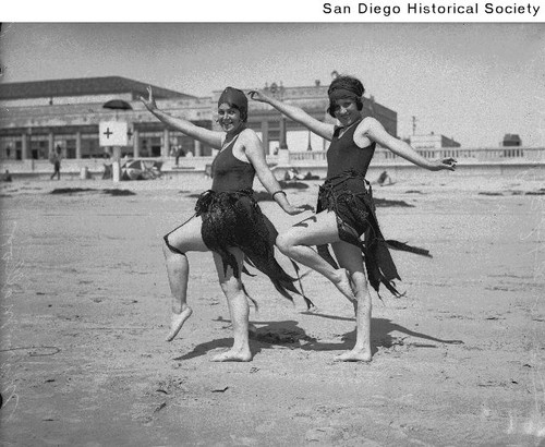Bobbie Harmon and Mary Malloy posing on a beach wearing bathing suits adorned with kelp