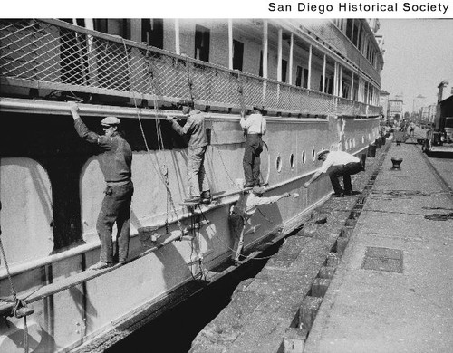 A group of men painting the side of a ship