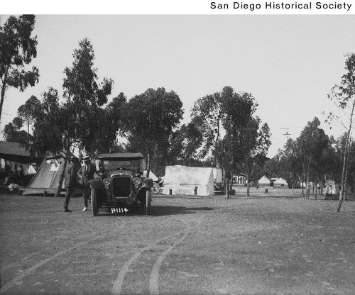 Two men by an automobile with tents in the background
