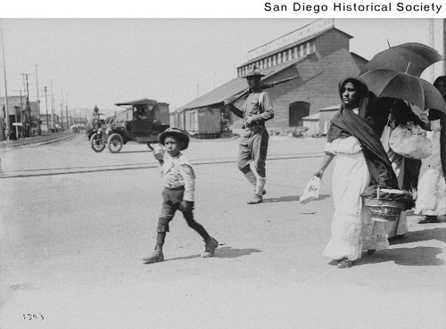 Mexican refugees walking under the guard of a US Soldier along a street in San Diego