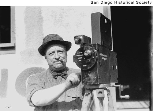 A man posing with a hand-cranked motion picture camera