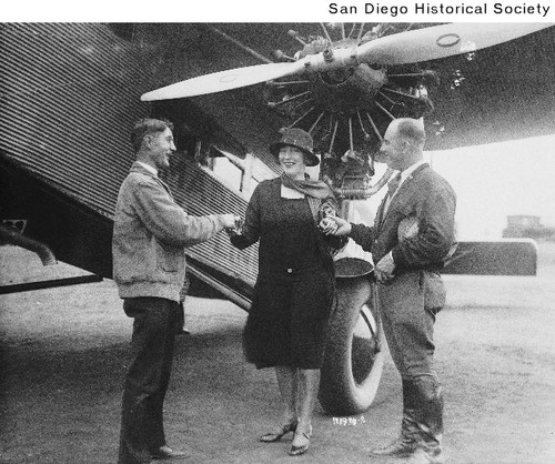 Two men and Miss Ellis standing near a Maddox Airlines Ford plane at Mahoney's Field