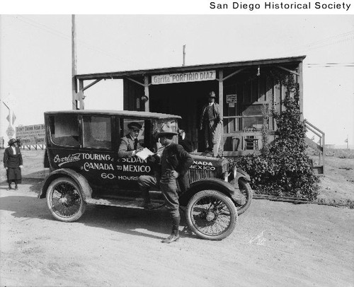 The driver of the Overland Touring Sedan handing a book to a Mexican police officer at the U.S.-Mexico border