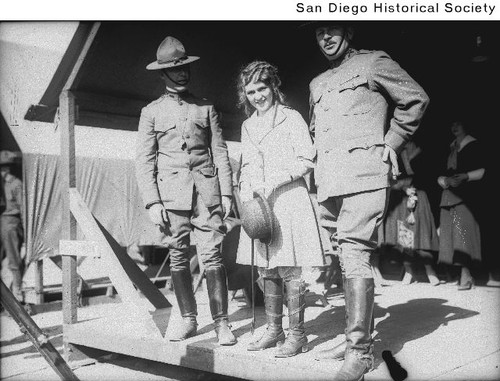Actress Mary Pickford standing with two army officers on a covered wooden platform