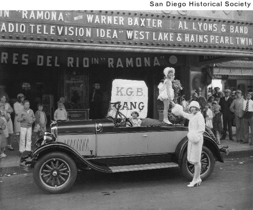 A young girl standing on the back of a 1928 Durant automobile parked in front of a movie theater