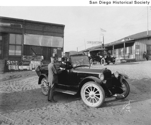 A Customs officer writing in a book as a man in an automobile watches at the U.S.-Mexico border