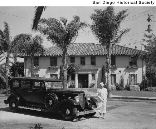 A woman standing in front of a Packard automobile parked in front of a house