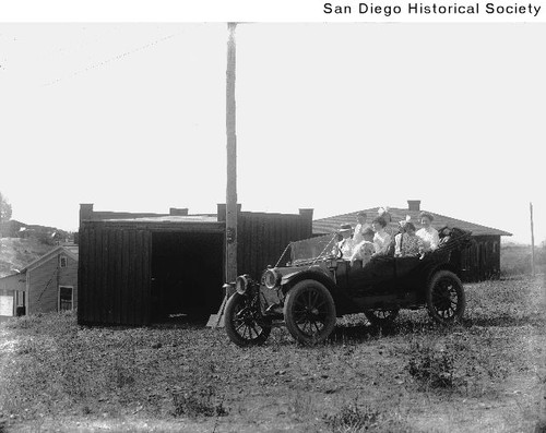 Group of people and a dog in an automobile parked in front of a shed