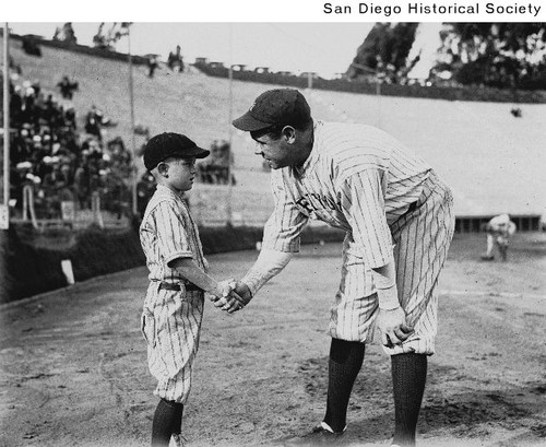 Babe Ruth in a baseball uniform shaking hands with a small boy