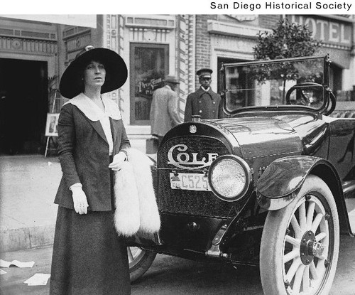 Edith Story standing in front of her Cole automobile, with her chauffeur in the background