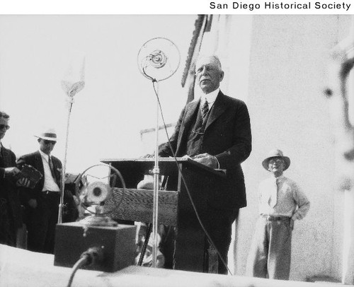 George Marston speaking into a microphone at the dedication of the Serra Museum