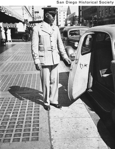 Marston's Department store doorman Charles Walker holding open the door of an automobile outside the store