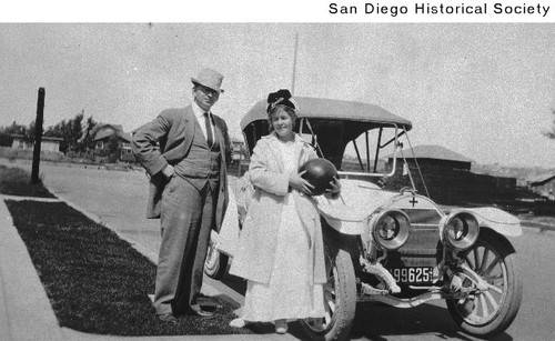 A man and a woman holding a ball standing in front of a parked automobile
