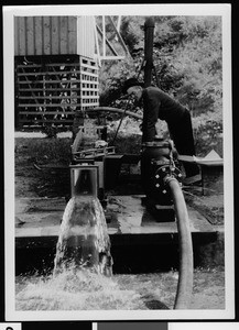 Department of Public Works employee checking flow measurements on the Venturi flume, spilling water to the ground, ca.1930