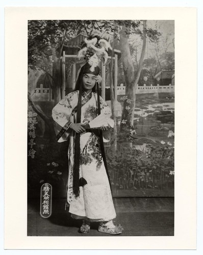 Actor as a scholar in classical costume with elaborate headdress holding a folding fan /