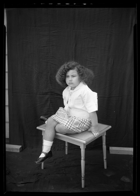 Portrait of girl in plaid skirt sitting on table