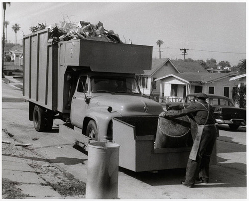 Sanitation worker disposing trash into a front loading truck in Santa Monica, February 7, 1956