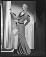 Peggy Hamilton modeling a full length dress with dolman sleeves and fur epaulettes, 1933