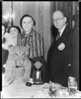 Peggy Hamilton, standing next to Ethel and Grace Bush, holds a lion cub at a Lions Club luncheon, Los Angeles, 1931-32