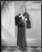 Peggy Hamilton modeling a black velvet dinner gown and metallic brocade jacket, 1930