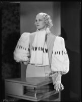 Peggy Hamilton modeling an evening gown with wide fur sleeves, 1933