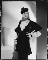 Peggy Hamilton modeling an Adrian gown with ruffles at the wrists and collar and a beret hat, 1933